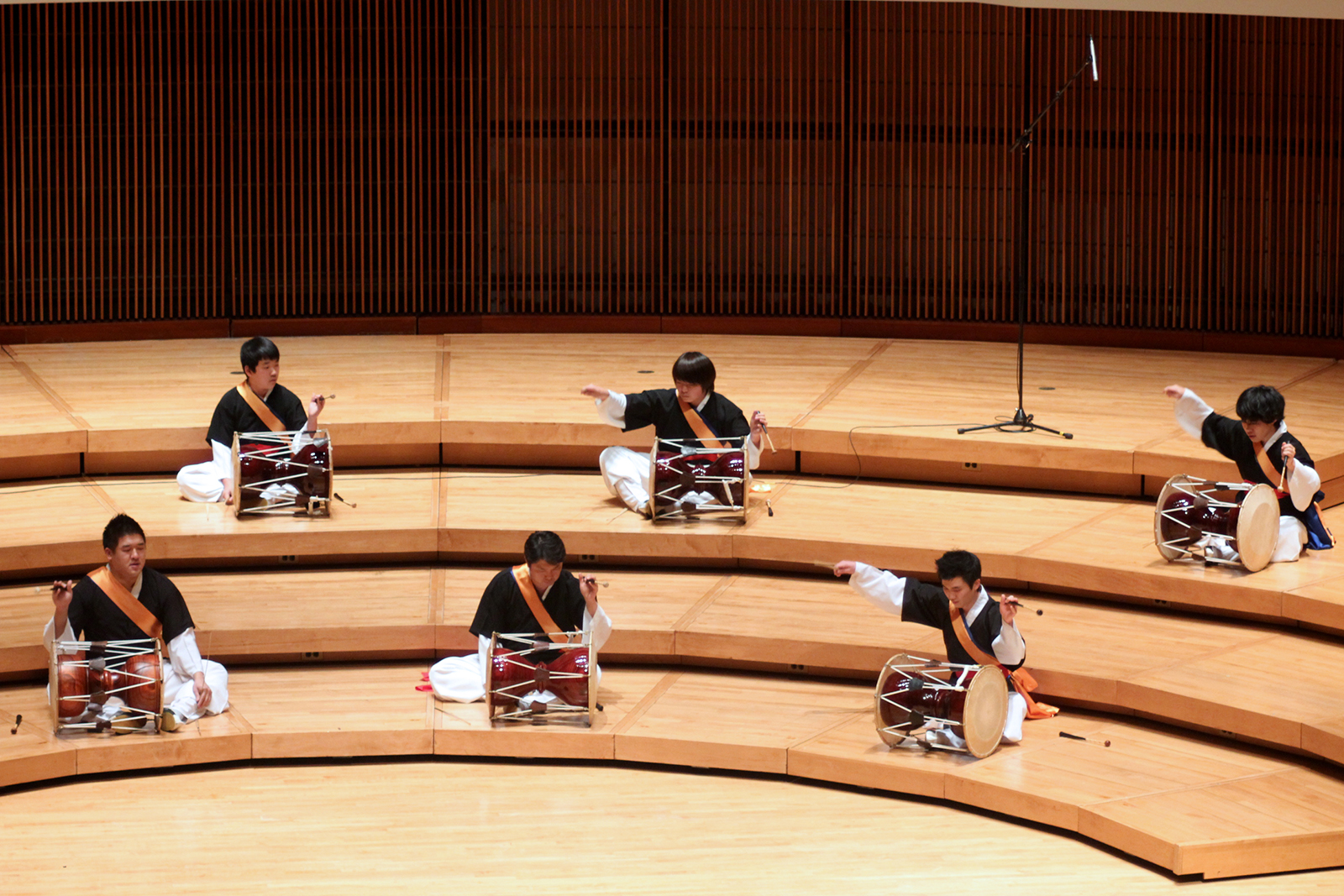 Members of the UMD Korean Percussion Ensemble play hourglass drums on stage.
