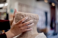 Hands shaping a face out of clay.