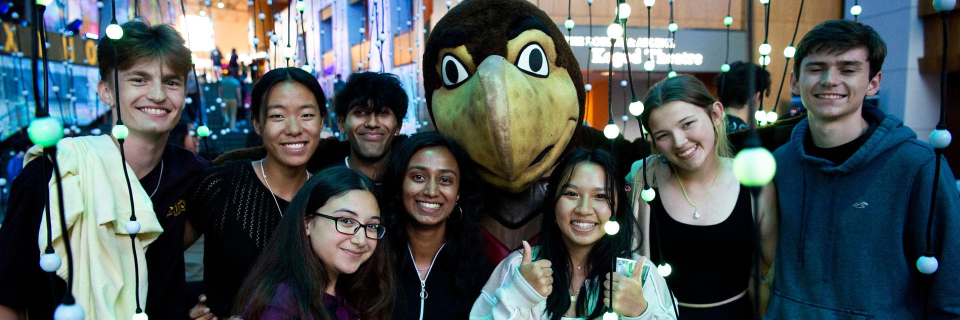 Eight students smile as they pose with Testudo in a light installation.