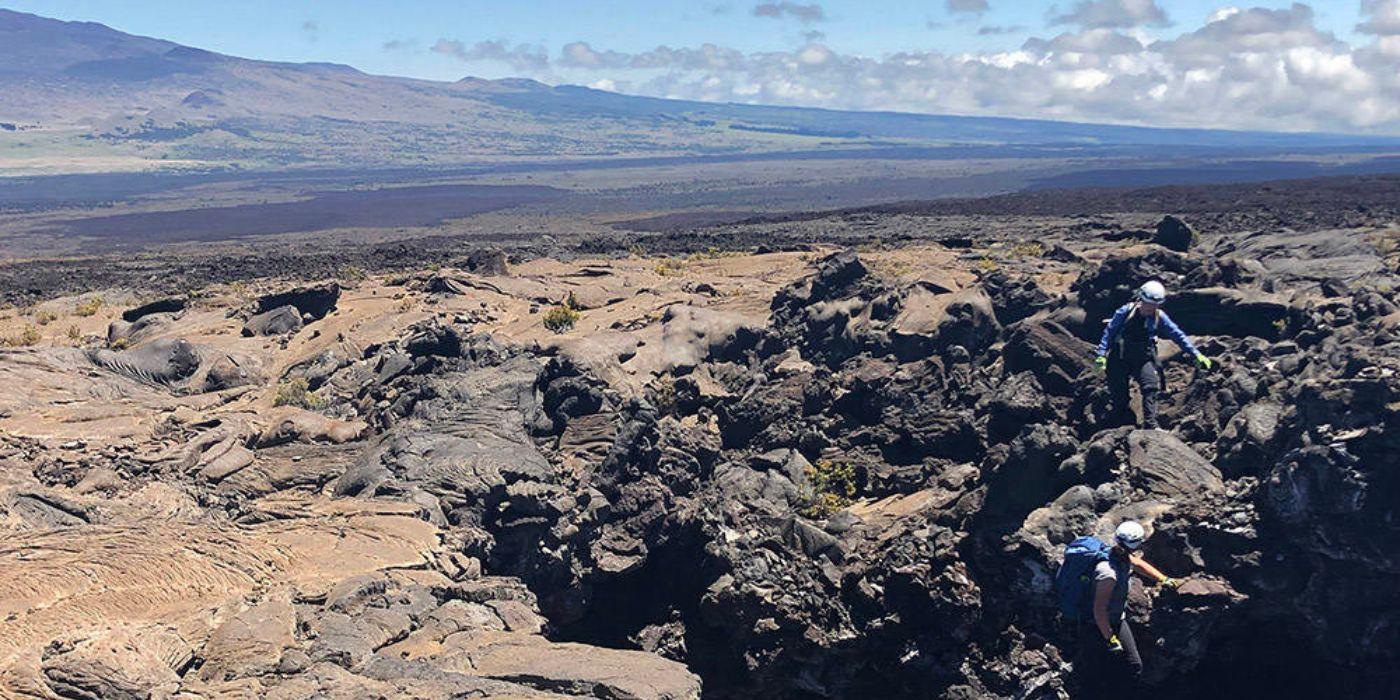 Two people explore rocks on a vast mountainous landscape. 