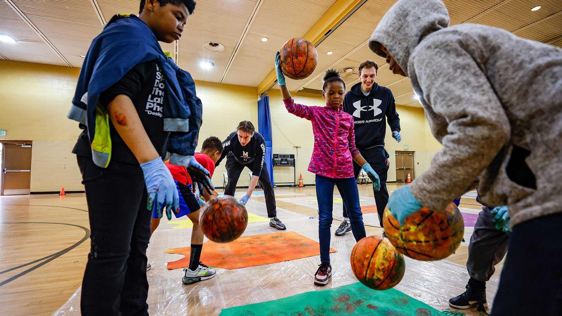 Basketball players and children bounce paint-smeared basketballs.