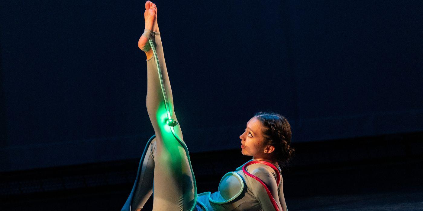 A dancer watches a small robot attached to her costume navigate up her leg.