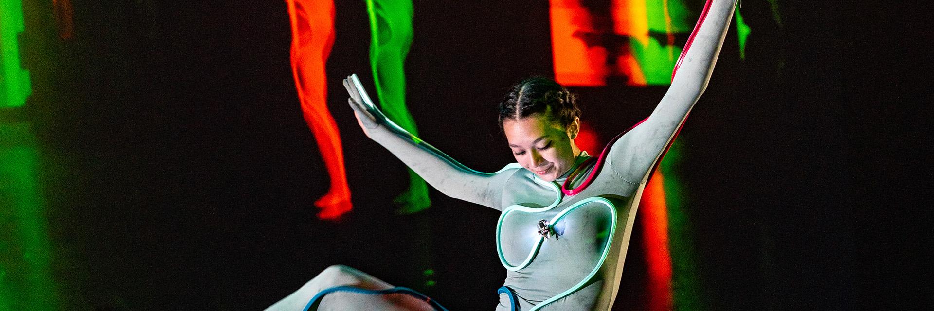 A female dancer wears a unitard track with a small robot navigating around her torso.
