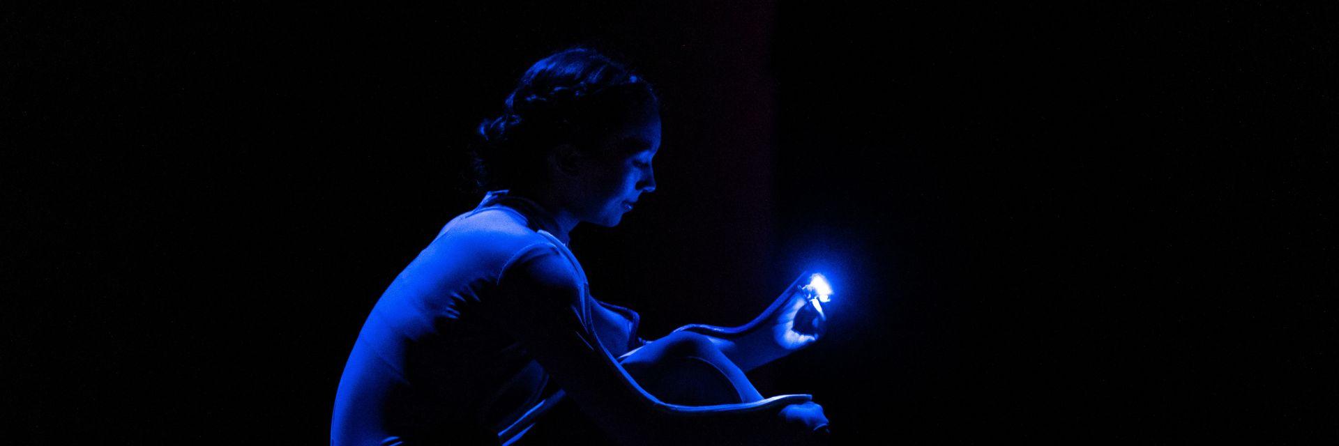 A dancer on a dark stage examines a tiny robotic sensor.