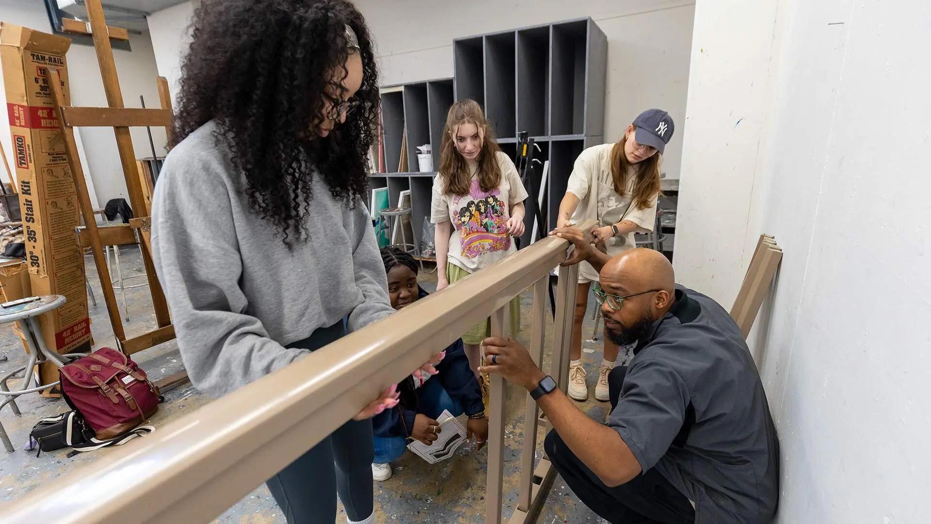Assistant Professor Brandon Donahue-Shipp helps students assemble a railing for an obstacle course composed of reused or surplus materials.