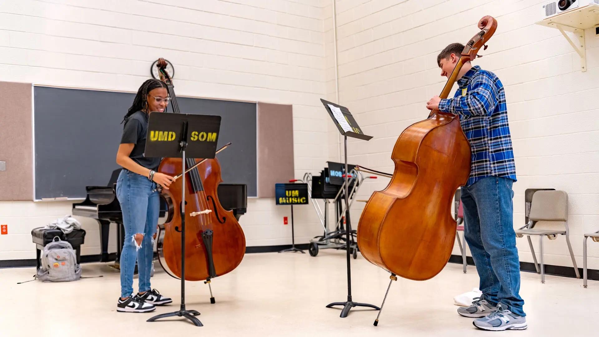Two students play bass in a music classroom.