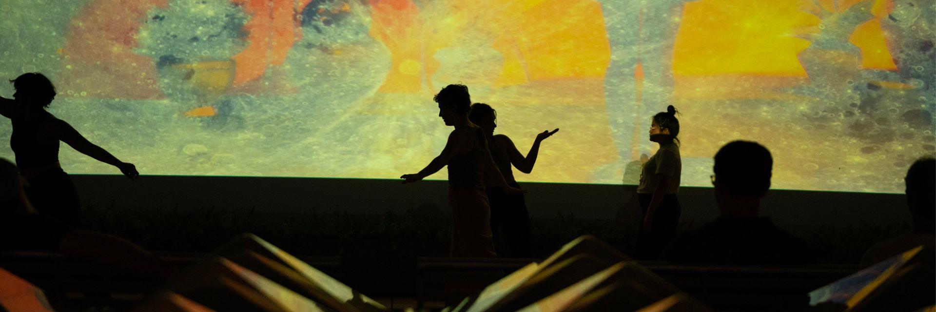 People dance in front a colorful screen.