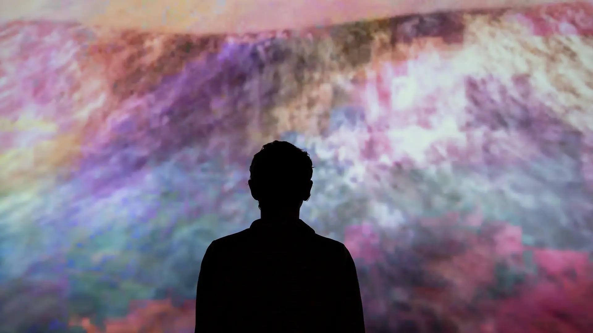 A person stands in front of a colorful, animated artwork.