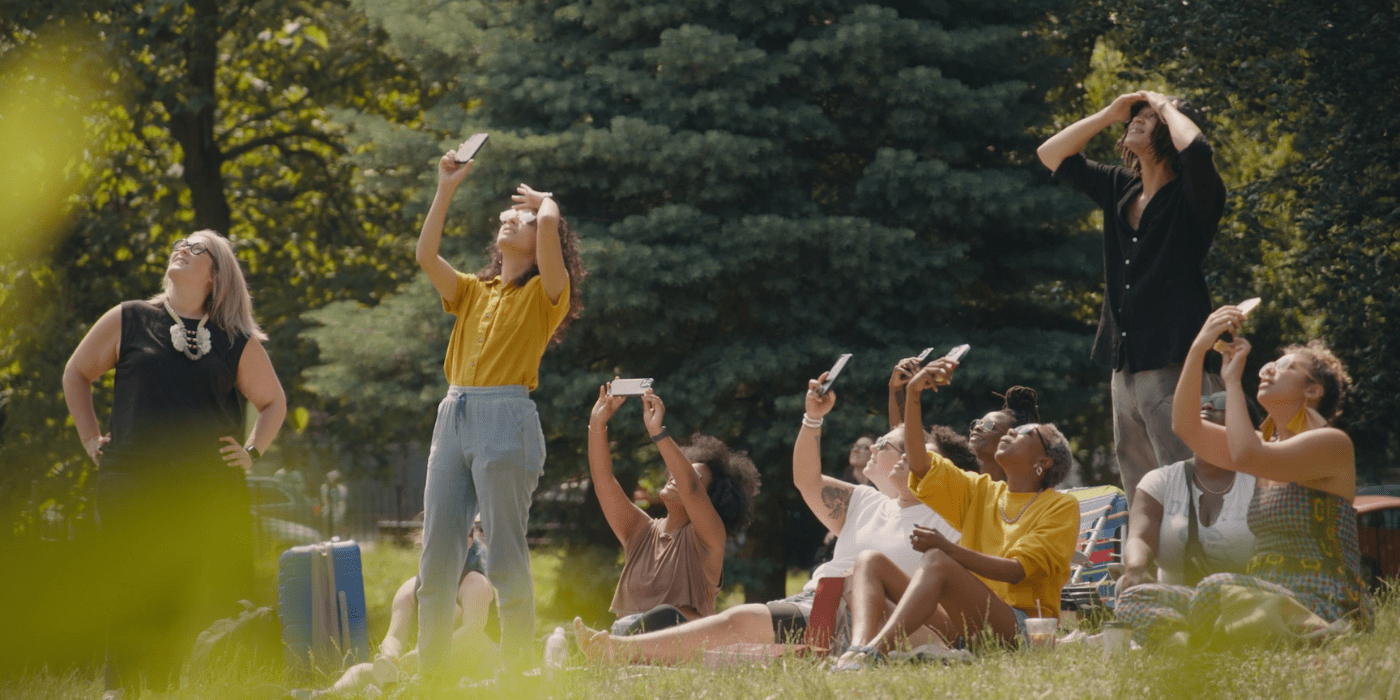 A group of people sitting outside wearing solar eclipse glasses and looking up at the sky.